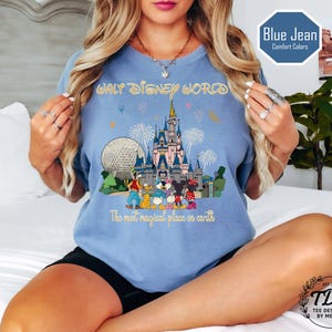 May include: A light blue t-shirt with a colourful graphic of Cinderella's castle, Spaceship Earth, and Disney characters. The text "WALT DISNEY WORLD" and "The most magical place on earth" are printed on the shirt.