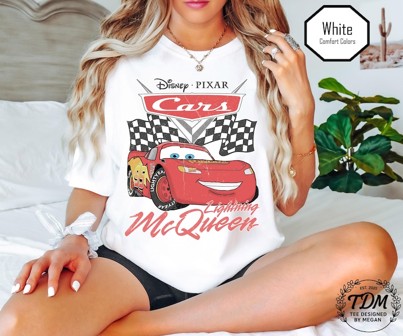 Puede incluir: Camiseta blanca con un dise&ntilde;o de Rayo McQueen de Cars de Disney Pixar. El dise&ntilde;o incluye el logotipo de Cars, banderas a cuadros y el texto "Lightning McQueen". La camiseta tambi&eacute;n tiene el texto "White Comfort Colors".