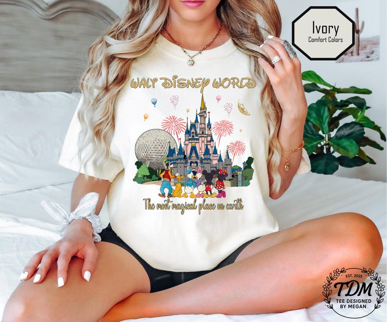 May include: Ivory t-shirt with a graphic of Cinderella's castle, Spaceship Earth, and Disney characters. The text "WALT DISNEY WORLD" and "The most magical place on earth" are printed on the shirt. The shirt is a comfort color.