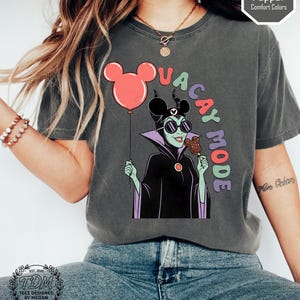 K&ouml;nnte beinhalten: Dunkelgraues T-Shirt mit einem Cartoon von Maleficent, die einen Mickey Mouse-Ballon und ein Eis h&auml;lt. Der Text "VACAY MODE" ist &uuml;ber der Figur angeordnet. Das Shirt tr&auml;gt den Text "Pepper Comfort Colors" und "TDM Tees Designed by Megan".