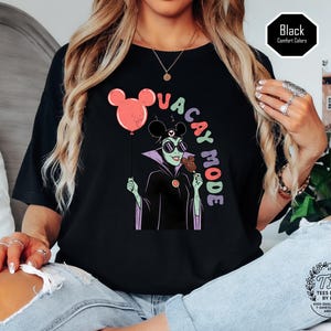 K&ouml;nnte beinhalten: Schwarzes T-Shirt mit einem Cartoon-Motiv einer gr&uuml;n geh&auml;uteten Figur mit Sonnenbrille, die ein Eis und einen Mickey-Mouse-Ballon h&auml;lt. Der Text "VACAY MODE" ist in bunten Buchstaben gehalten. Das Shirt ist mit "Comfort Colors" gekennzeichnet.