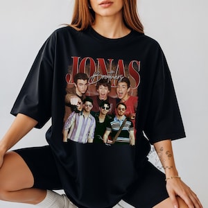 May include: A black oversized t-shirt featuring a graphic print of the Jonas Brothers. The design includes the text JONAS in large red letters and Brothers in script, with a collage of the band members in various outfits and poses.