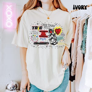 May include: Ivory t-shirt with a graphic design including the text "ONE TREE HILL", "TRC", "RED BEDROOM RECORDS", and other phrases. The design features a car, a heart, and a traffic light. The shirt has a relaxed fit.