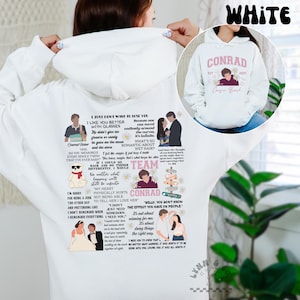 Peut inclure: Sweat à capuche blanc avec le mot "CONRAD" et un graphisme d'une personne et de fleurs. Le sweat à capuche comporte également diverses citations et images d'une émission. Le mot "WHITE" est en haut.