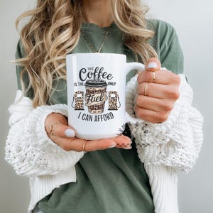 May include: White ceramic coffee mug with the text "This Coffee is the Only Fuel I Can Afford". The mug features a coffee cup and gas pump design with a leopard print pattern. The mug has a large handle.