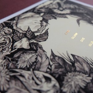 May include: A black and white illustration of flowers with the text "Live Slow Die Old" printed in gold on a cream background.