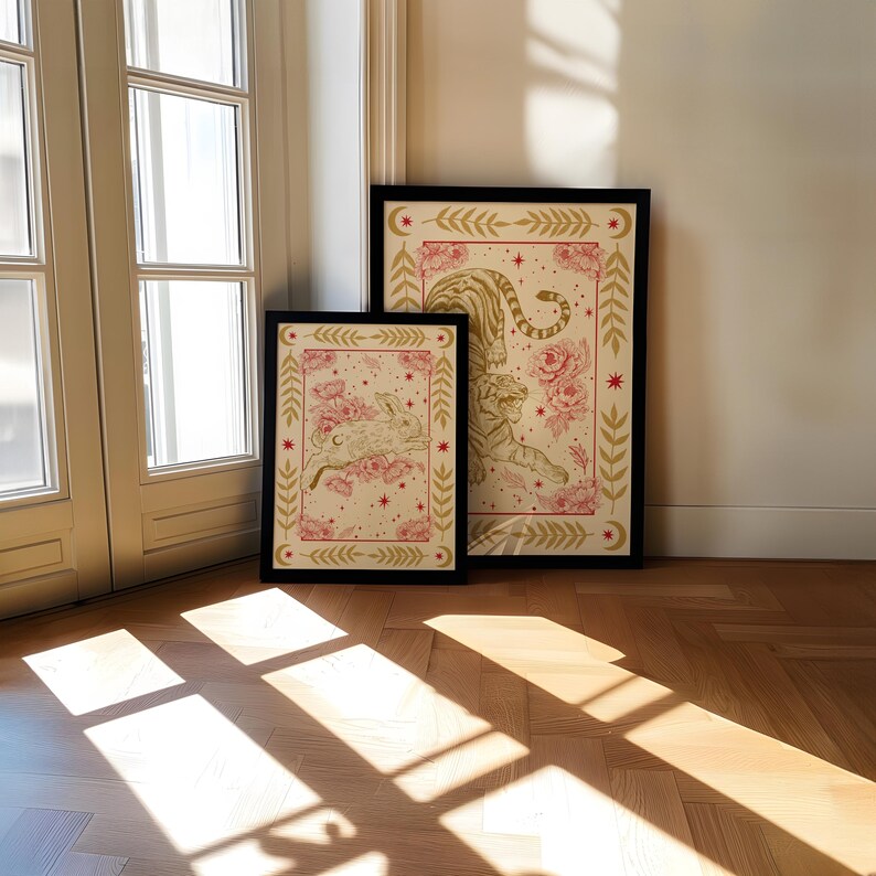 May include: Two framed prints with a cream background and gold and pink floral designs. The larger print features a tiger with a floral crown and the smaller print features a rabbit with a floral crown.