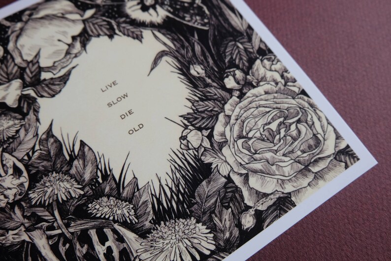 May include: Black and white illustration of flowers and foliage with the text "Live Slow Die Old" in the centre.