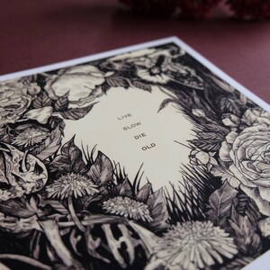 May include: Black and white illustration of flowers and foliage with the text "Live Slow Die Old" in the centre.