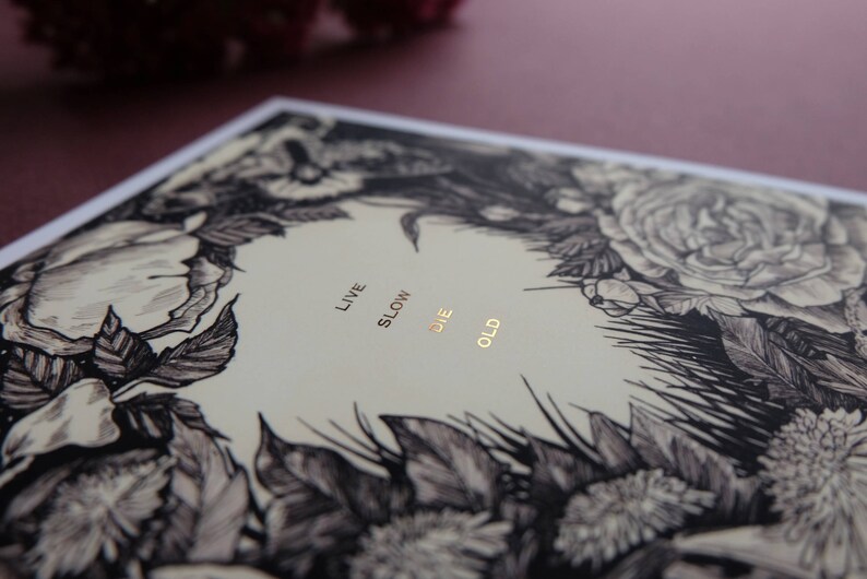 May include: A black and white floral illustration with gold foil lettering that reads "Live Slow Die Old".