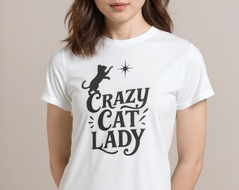May include: White t-shirt with the text "Crazy Cat Lady" in a black, stylized font. A black cat silhouette is above the text, reaching for a star. The shirt is a crew neck and short-sleeved.