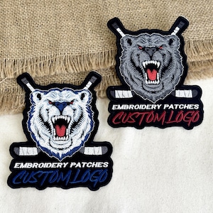 May include: Two embroidered patches featuring a bear with hockey sticks. One patch has a white bear with blue accents, the other a gray bear. Both have the text "EMBROIDERY PATCHES CUSTOM LOGO" in a curved banner.