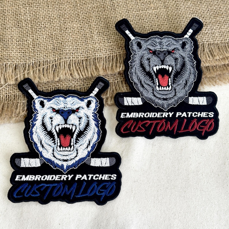 May include: Two embroidered patches featuring a bear with hockey sticks. One patch has a white bear with blue accents, the other a gray bear. Both have the text "EMBROIDERY PATCHES CUSTOM LOGO" in a curved banner.