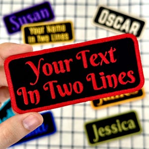 May include: Black rectangular patch with red trim and the text "Your Text In Two Lines" in red script. Other patches with names like "Susan" and "Oscar" are visible in the background. The patches are on a checkered surface.