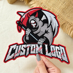 May include: An embroidered patch featuring a grim reaper figure with red eyes, a grey hooded cloak, and a scythe. The figure is positioned above the text CUSTOM LOGO, which is rendered in a bold, distressed grey font with red accents and a red border.