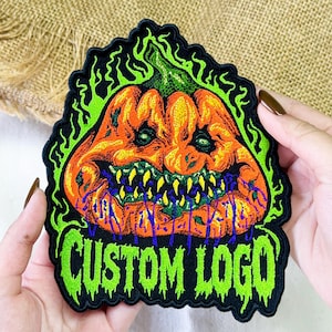 May include: An embroidered patch featuring a central orange pumpkin with a menacing expression, sharp yellow teeth, and purple dripping accents. The pumpkin is surrounded by bright green flames, with the text CUSTOM LOGO in green at the bottom.