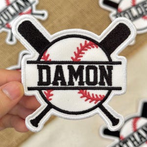 May include: Embroidered baseball patch with the name "DAMON" in black block letters. The patch features a white baseball with red stitching, crossed black baseball bats, and a white border.