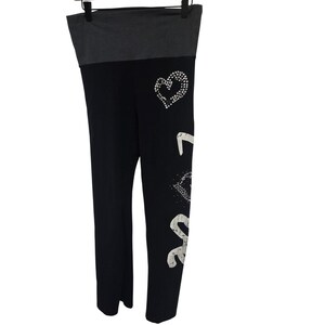 May include: Black leggings with a gray waistband. The left leg features the word "LOVE" in a white, sparkly font, with a heart design above. The leggings are hanging on a black hanger.