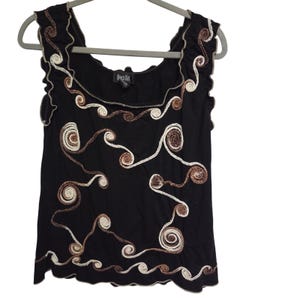 May include: Black sleeveless top with a square neckline and a wavy, embroidered design in cream and brown. The top has a scalloped edge and is hanging on a gray hanger. The brand name "Dress Fat" is visible on the tag.