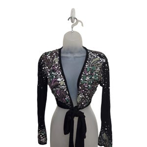 May include: Black bolero jacket with long sleeves and a tie closure. The jacket is embellished with sequins in shades of silver, purple, and green, arranged in a floral pattern. The jacket is displayed on a mannequin.