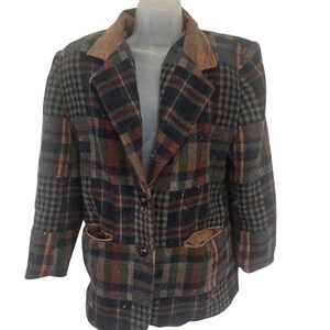 May include: A long-sleeve blazer featuring a multi-colored plaid pattern in shades of dark green, navy blue, and rust orange. The garment includes a tan-colored collar and matching tan-colored pocket trim, with two dark buttons centered on the front.