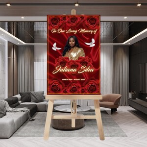 May include: A memorial sign on a wooden easel. The sign features a portrait of a woman, surrounded by red roses and the text "In Our Loving Memory of Juliana Silva". The sign includes the dates "March 1990 - August 2025".