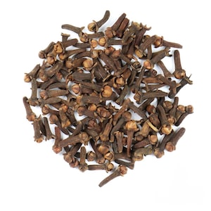 May include: A pile of dried cloves, a common spice, is displayed against a white background. The cloves are a deep brown color, with small, rounded heads and elongated stems. The arrangement is dense, with many cloves overlapping.