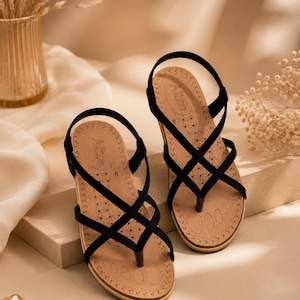 May include: A pair of black sandals featuring thin, crisscrossing straps and a thong-style toe post. The tan footbed is printed with the brand name Alize, a geometric floral pattern, and the number 8, indicating the size on the insole.