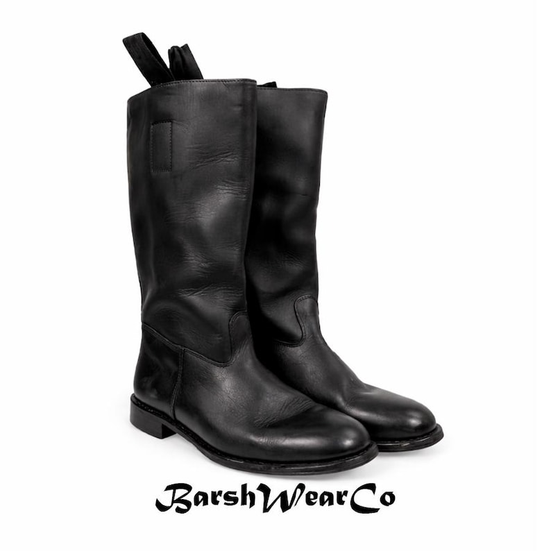 May include: A pair of tall, black leather boots with a pull tab at the top. The boots have a smooth finish and a low heel. The brand name "BarshWearCo" is printed at the bottom of the image.