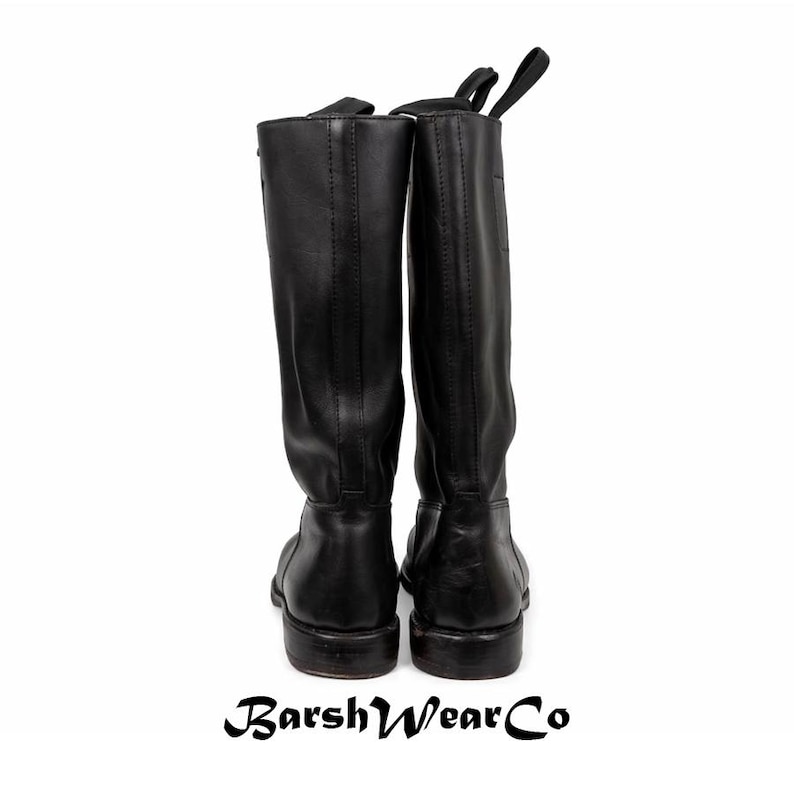 May include: A pair of black leather riding boots. The boots are tall, with a smooth finish and a pull tab at the top. The soles are dark, and the boots are set against a white background. The brand name "BarshWearCo" is at the bottom.