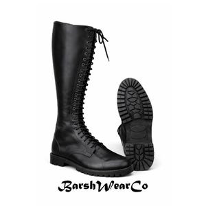 May include: Black knee-high lace-up boots with a lug sole. The boots are made of leather and have a round toe. The sole of one boot is visible, showing the tread pattern. The brand name "BarshWearCo" is at the bottom.
