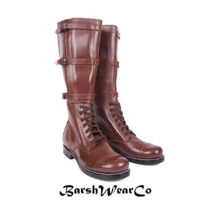 Pode incluir: Um par de botas de couro castanho com design de atacadores e várias correias com fivelas. As botas têm cano alto e bico arredondado. A marca "BarshWearCo" está impressa na parte inferior da imagem.