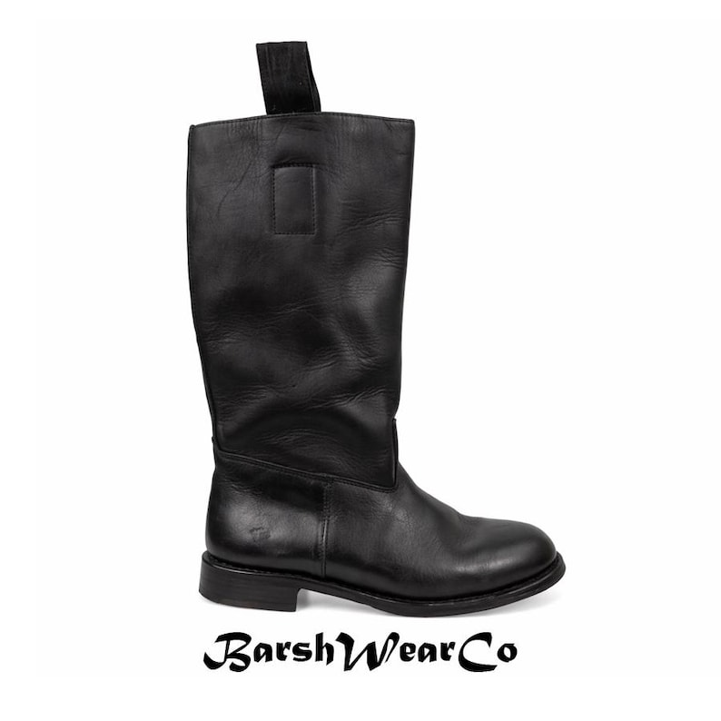 May include: A black leather knee-high boot with a pull tab at the top. The boot has a rounded toe and a low heel. The brand name "BarshWearCo" is printed at the bottom of the image.