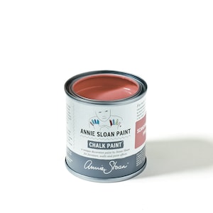 Könnte beinhalten: Eine Dose Annie Sloan Chalk Paint in der Farbe Skandinavisch Rosa. Die Dose ist silberfarben mit einem weißen Etikett und zeigt eine Cartoon-Illustration eines Kindes mit bunten Händen.