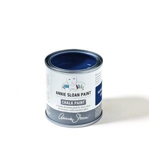Könnte beinhalten: Eine Dose Annie Sloan Chalk Paint in der Farbe Napoleonblau. Die Dose ist silberfarben mit einem weißen Etikett und zeigt ein Kind mit bemalten Fingerspitzen.