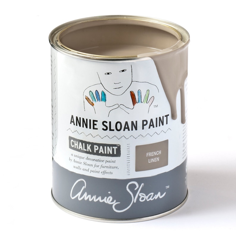 Puede incluir: Una lata de pintura a la tiza Annie Sloan en el color Lino Franc&eacute;s. La lata es gris con una etiqueta blanca y presenta una ilustraci&oacute;n de dibujos animados de una persona con manos de colores. La etiqueta tambi&eacute;n incluye el texto "Chalk Paint" y "French Linen".