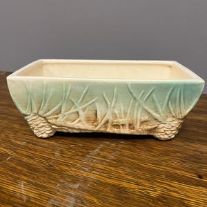 May include: A white ceramic mug with a black handle and the text "But First, Coffee" in a bold, black font. The mug is set against a blurred background, suggesting a cosy setting.