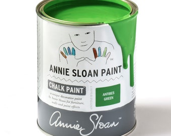 Puede incluir: Una lata de pintura a la tiza Annie Sloan en verde Antibes. La pintura es de un color verde vibrante, con algo de pintura goteando por el costado de la lata. La lata tiene una etiqueta blanca con el nombre de la marca y un dibujo de una persona.