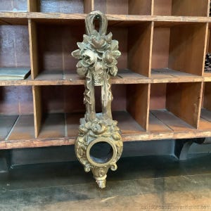 Puede incluir: Aplique de pared antiguo de color dorado con detalles florales y de cinta. El aplique presenta una abertura circular en la parte inferior y un lazo en la parte superior para colgar. El diseño incluye múltiples rosas y una estética vintage decorativa.