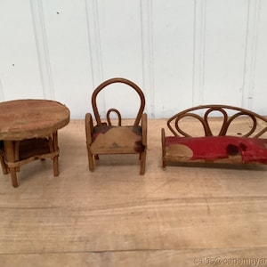May include: A miniature wooden dollhouse furniture set with a round table, a chair, and a couch. The furniture is made of wood and has a rustic look. The couch has a red fabric cushion.