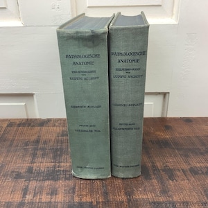 May include: Two vintage books with green covers. The text "PATHOLOGISCHE ANATOMIE" is printed on the spine. The books are labeled "SIEBENTE AUFLAGE" and "ZWEITER BAND SPEZIELLER TEIL" and "ERSTER BAND ALLGEMEINER TEIL".