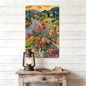 May include: A metal sign depicting a painting of a floral still life with a road and landscape in the background, in the style of Van Gogh. The artwork features a vase of flowers with a warm colour palette and visible brushstrokes.