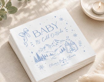 May include: A stack of white paper napkins featuring blue ink illustrations of mountains, pine trees, baby bottles, snowflakes, and a bow. The text reads BABY It's Cold Outside, Oliver's Baby Shower, and the date 02.03.26 in a script font.