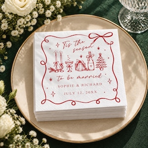 Op de afbeelding: Een stapel vierkante witte papieren servetten met een rode decoratieve rand en rode inktillustraties van kaarsen, een champagneglas, een cadeau, een fles en een boom. De tekst luidt: Tis the season to be married, SOPHIE & RICHARD, JULY 12, 20XX.