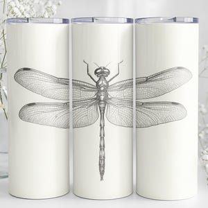 以下が含まれることがあります： 白の断熱タンブラー3個。黒と白のトンボのイラストが描かれています。各タンブラーの中央にトンボが配置され、羽を広げています。タンブラーには銀色の蓋が付いており、温かい飲み物と冷たい飲み物の両方に使用できます。