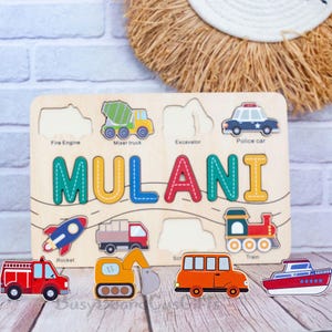 May include: Wooden puzzle with the name "MULANI" in colourful letters. The puzzle features vehicle shapes, including a fire engine, mixer truck, excavator, police car, rocket, truck, school bus, train, and boat. The puzzle is on a wooden surface.