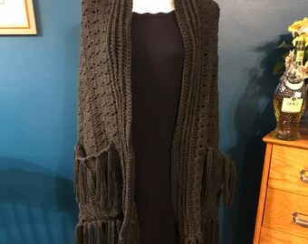 May include: A dark green crocheted shawl with fringe and pockets. The shawl is draped over a dress form.