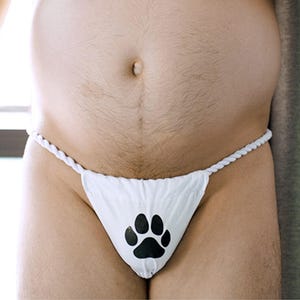 Puede incluir: Tanga blanco con un diseño de huella de pata negra. El tanga tiene una cintura de cuerda blanca trenzada. La ropa interior está hecha de un material suave y opaco.
