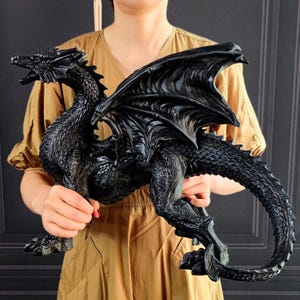 Peut inclure: Figurine de dragon noir détaillée, avec des ailes déployées et une gueule ouverte. La sculpture présente des écailles texturées et des détails d'ailes complexes. Objet décoratif sur le thème de la fantaisie.