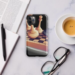Peut inclure: Coque de téléphone noire avec un motif d'échiquier et des pièces d'échecs blanches. L'étui a une finition brillante et est présenté sur une surface en marbre. Une tasse de café et des lunettes sont également visibles.